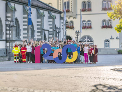 Gruppe feiert 120-jähriges Jubiläum vor historischem Gebäude. Menschen jubeln. Event.