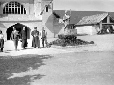 Historisches Foto: Gruppe von Personen vor Kirche mit Statue. Schwarzweiß-Aufnahme.