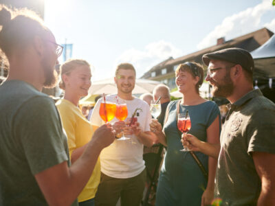 Gruppe feiert mit Aperol Spritz. Sommerliches Event, Getränke, fröhliche Menschen.
