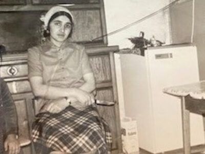 Schwarzweißfoto einer sitzenden Frau mit Kopftuch, kariertem Rock und Hemd. Vintage-Porträt.