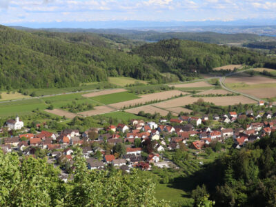 Panorama: Dorf, Felder, Wald und Hügel. Ländliche Szene mit roten Dächern und grüner Natur.